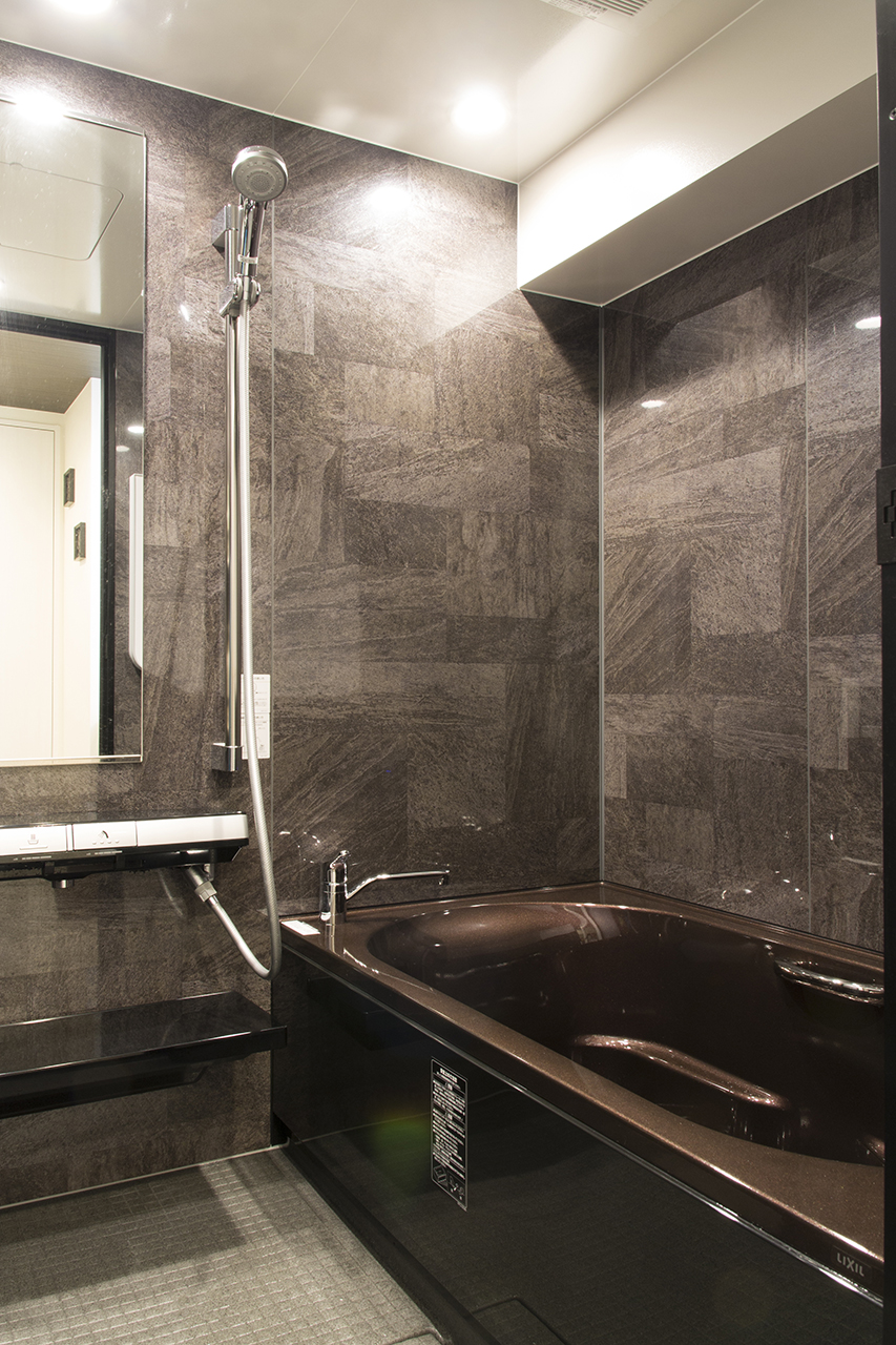 浴槽は思い切ってゴールドブラウンを採用。照明をダウンライトにすることで、暗色のコーディネートでも狭さを感じにくくなりました。
4面の鏡面組石グレーパネルが上質感をグッと押し上げます。-ライフスタイルに合せ浴室・水回りをリゾートホテル風にリフォーム-